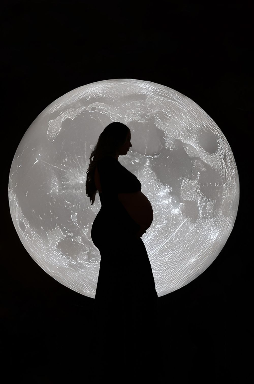 Silhouetted figures against dramatic moon backdrop in artistic maternity photography.