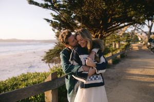Couple in casual clothes sharing affectionate moment along scenic coastal path at sunset.