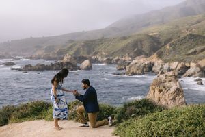A couple shares a romantic moment on a cliff overlooking the rugged Big Sur coastline in California.