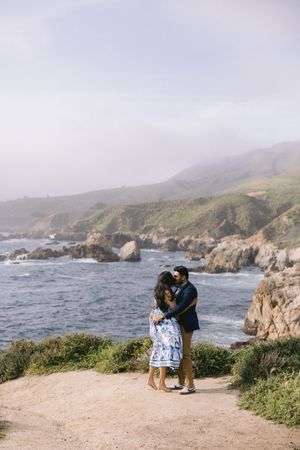 A couple embraces while admiring the rugged coastline views along Big Sur in California during an overcast day.
