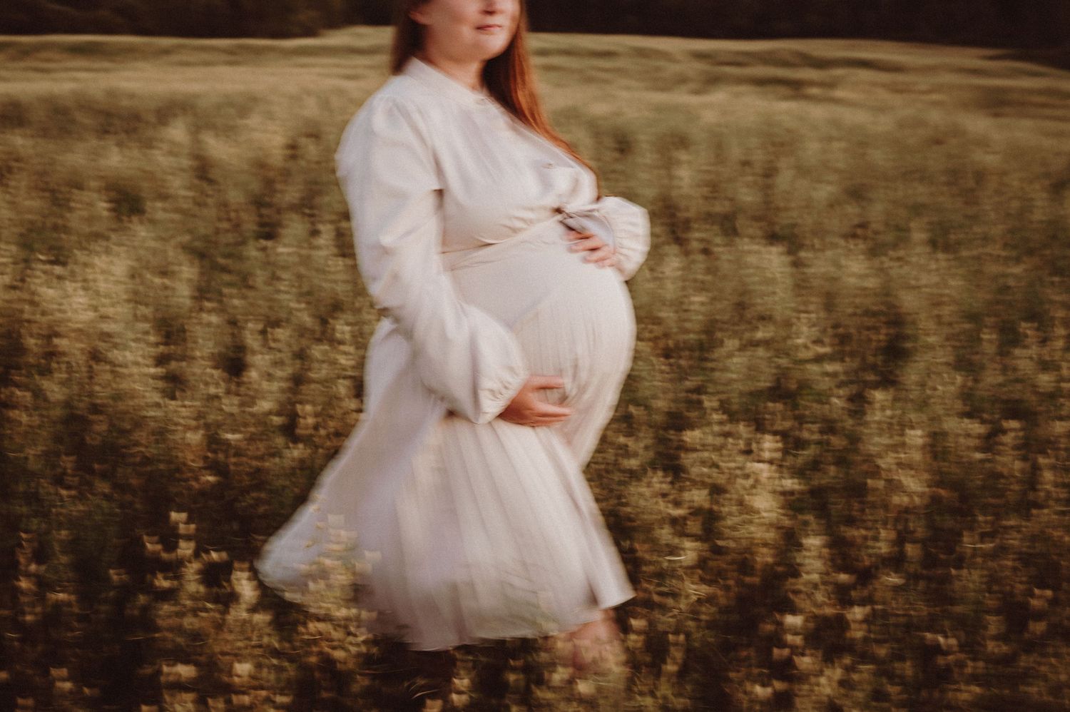 Une photo de maternité dans un champ doré montre une future maman en robe blanche fluide au coucher du soleil.
