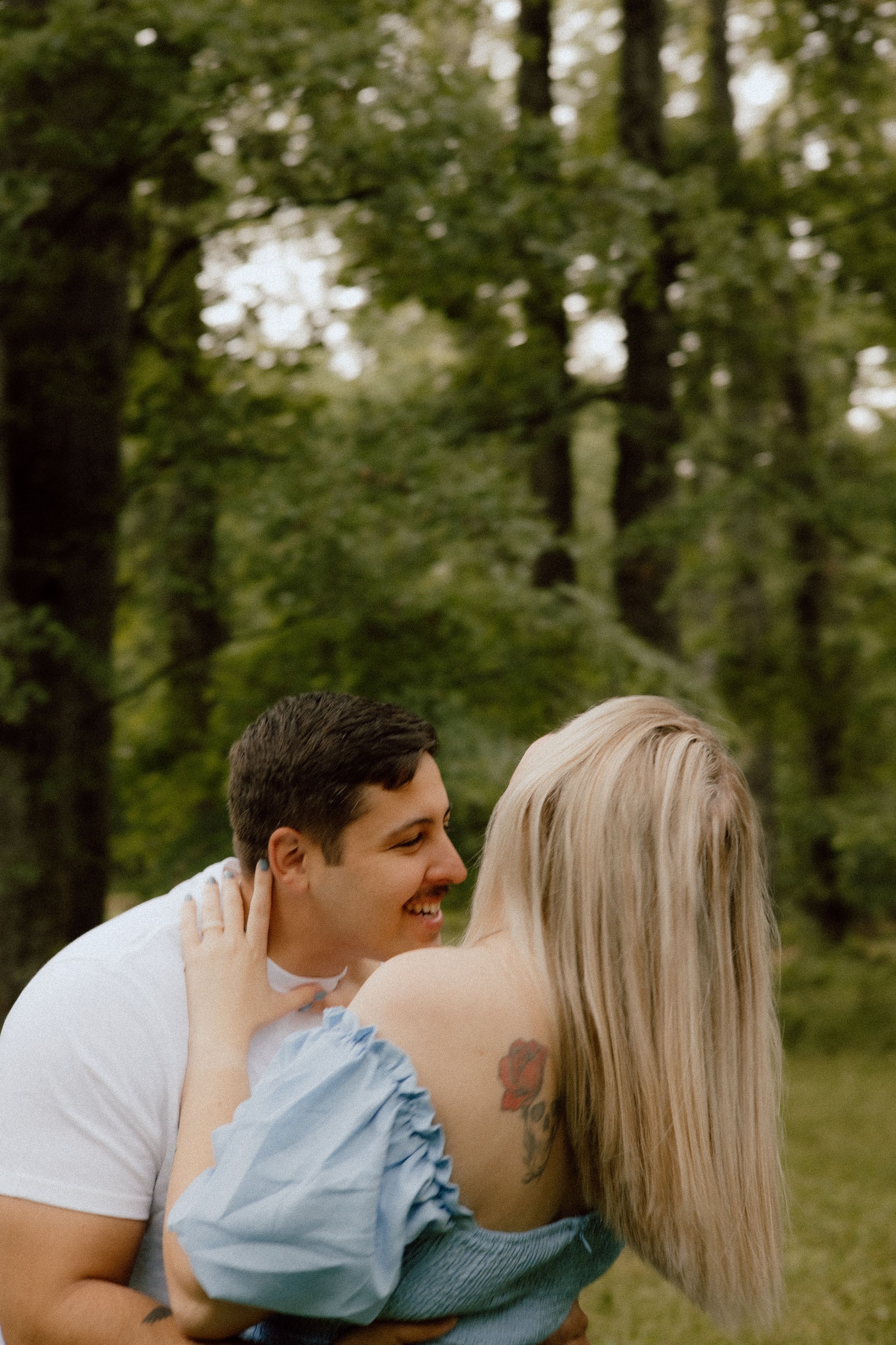 A tender moment between a couple against a lush green forest backdrop.