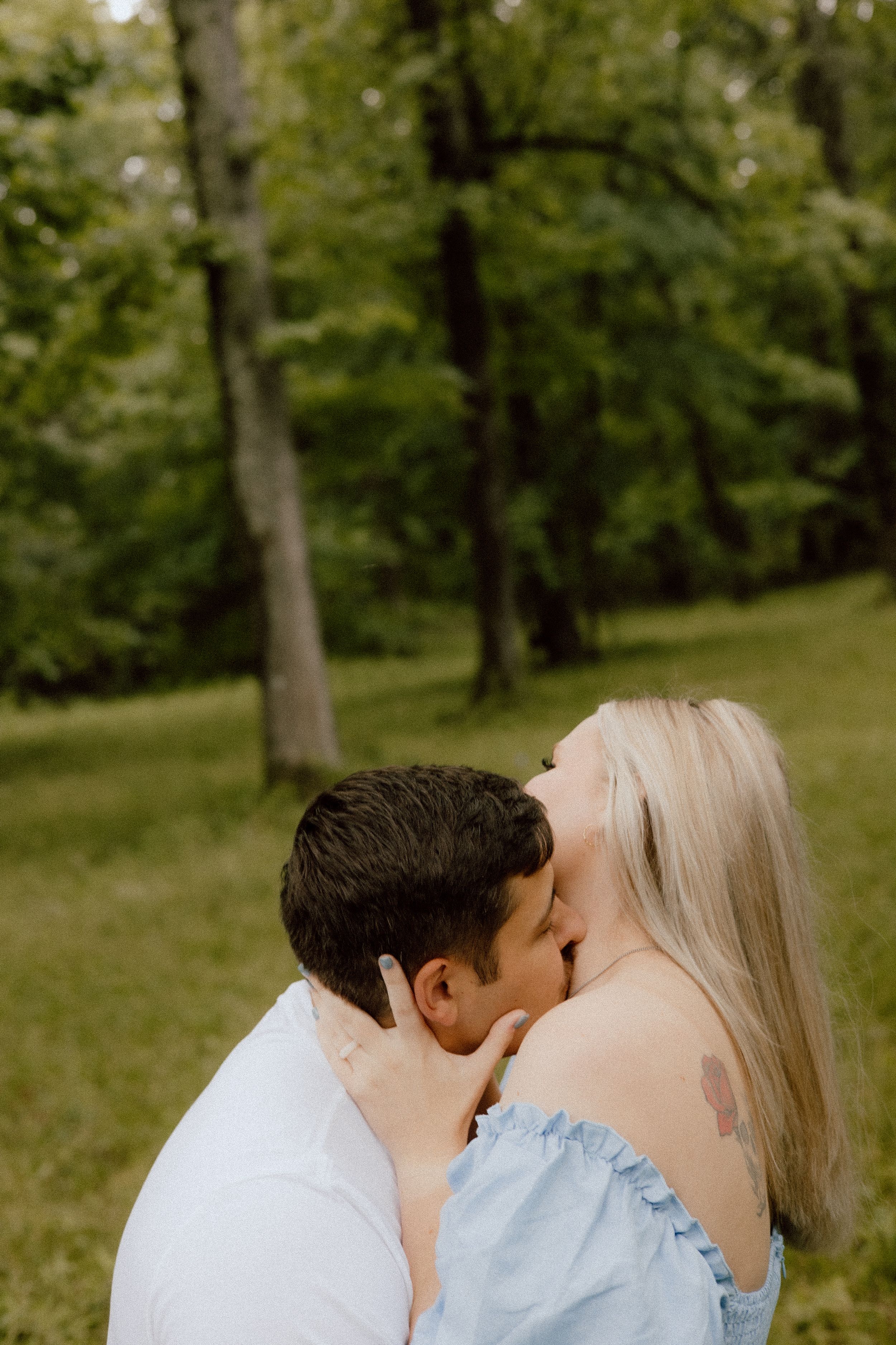A romantic moment between a couple in a green forest setting with soft natural lighting.