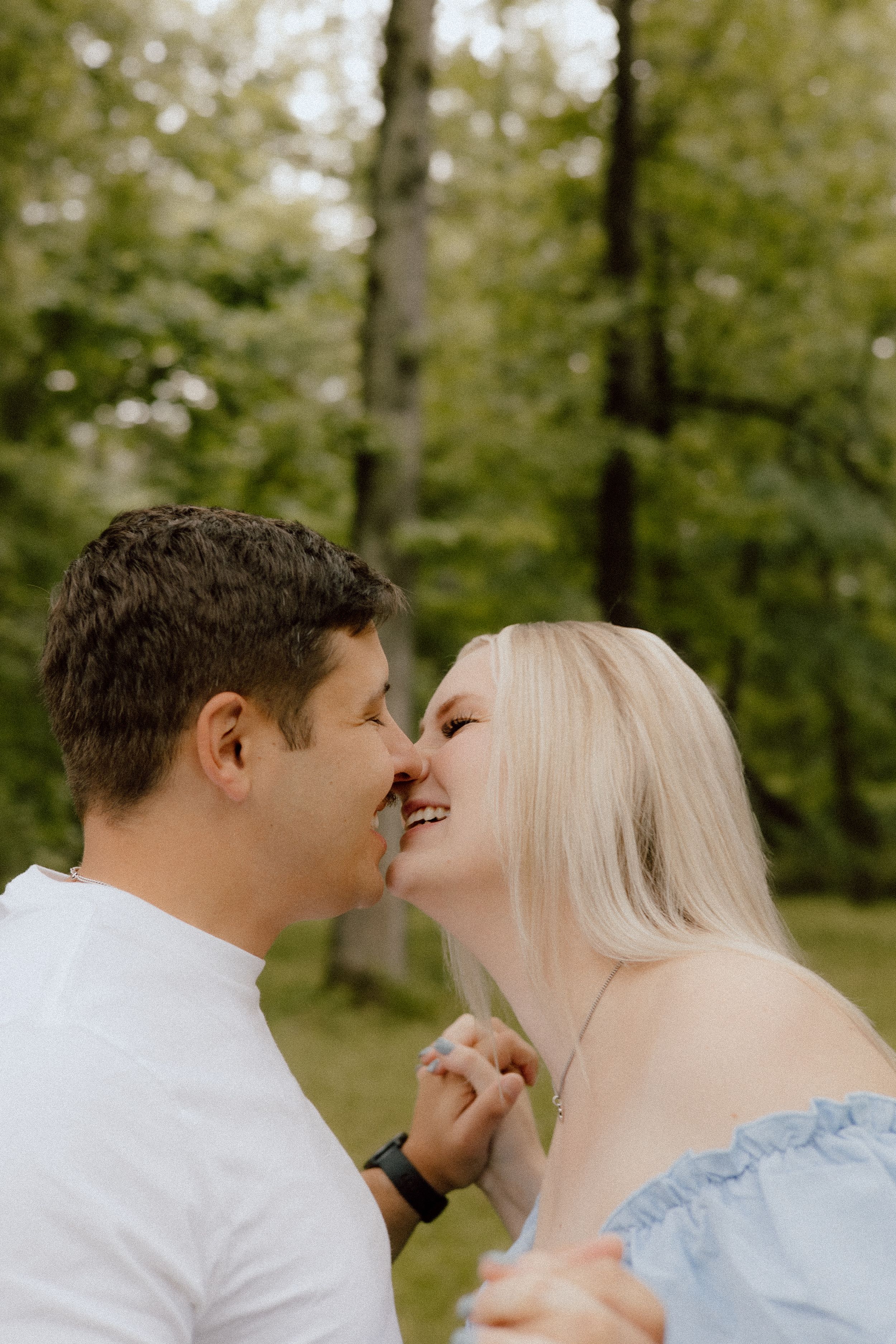 A romantic outdoor moment captured in the woods showing laughter and joy between two people.