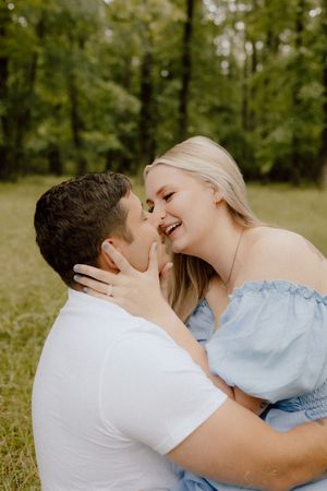 A romantic outdoor moment with couple laughing and sharing an intimate embrace in a sunlit forest setting.