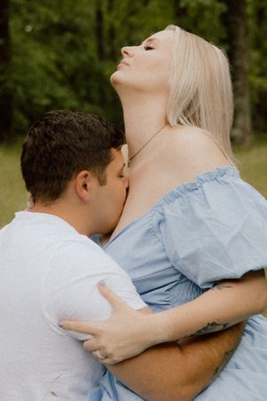 A romantic couple embraces outdoors with one wearing a white shirt and the other in a light blue dress.
