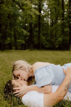 Romantic couple lying together in a lush green meadow surrounded by trees on a summer afternoon.