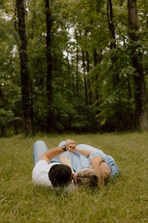 A couple lying together on grass in a peaceful woodland setting during golden hour.