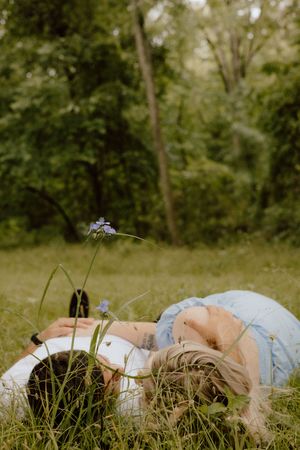 Person lying in tall grass on a summer day holding wildflowers in a dreamy outdoor setting.