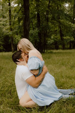 A romantic couple embrace while sitting in tall grass in a forest setting on a sunny day.