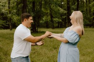 A couple stands together on grass during a heartfelt moment in a wooded outdoor setting.