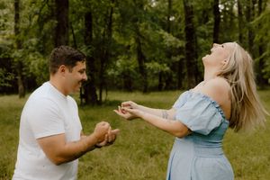 A couple shares a joyful moment during a proposal in a sunlit wooded area.