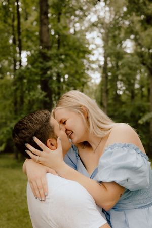 A romantic outdoor moment with a couple embracing and laughing together in a sunlit forest setting.