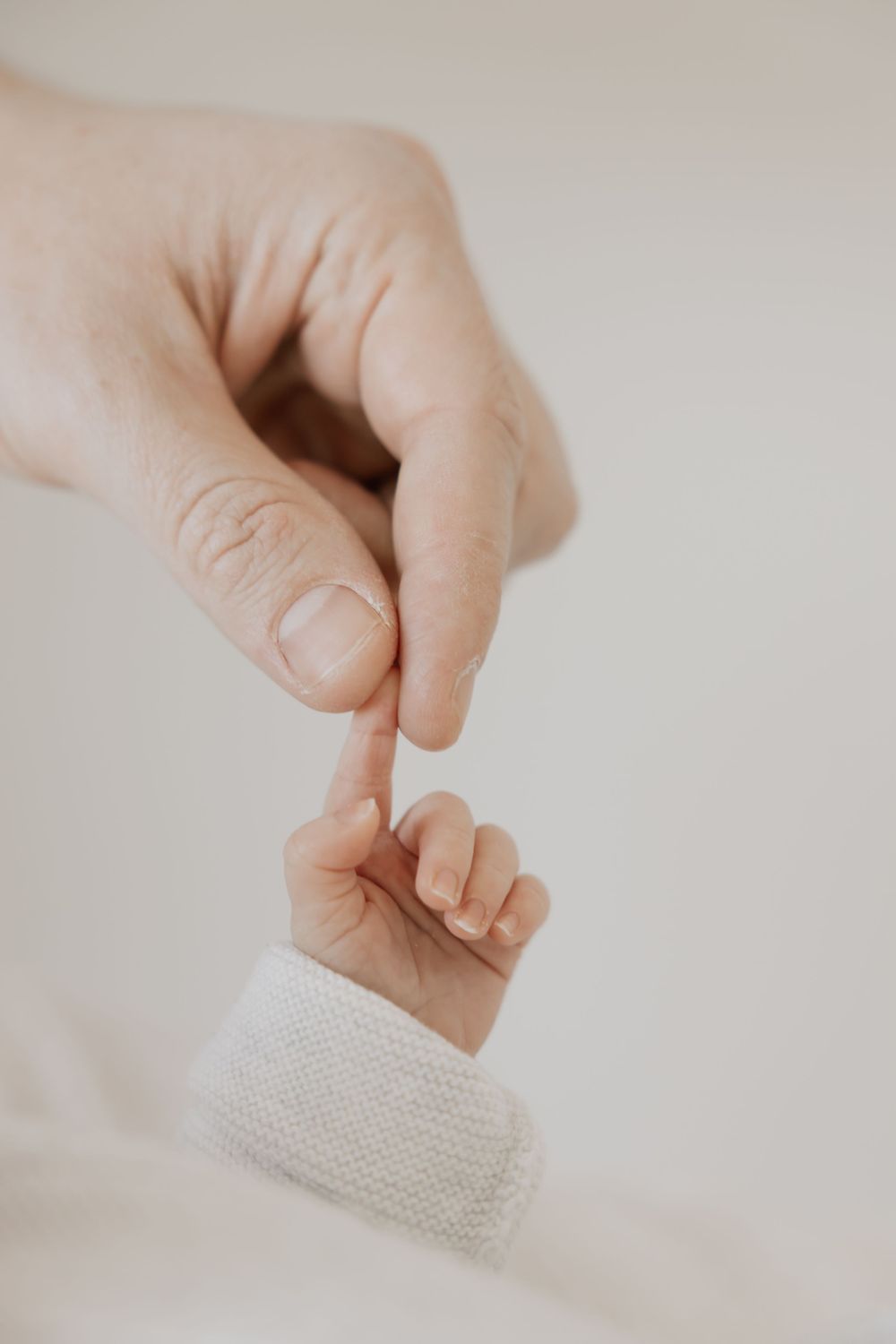 A gentle adult hand touching fingertips with a tiny newborn baby hand, symbolizing love and new parenthood.