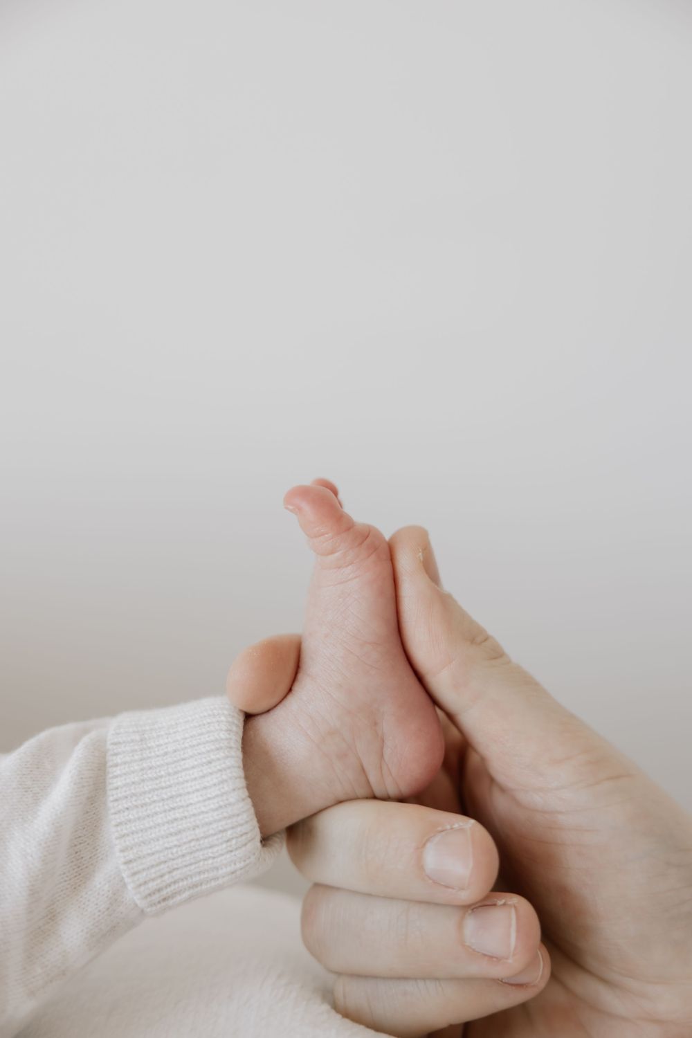 Adult hands gently cradling a newborn baby's tiny foot, symbolizing parental love and care.