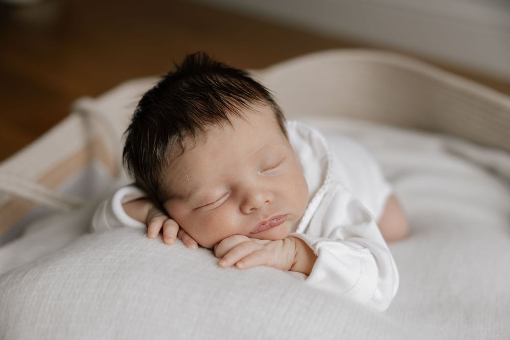 Sleeping newborn baby wearing white clothes rests peacefully on soft white bedding.