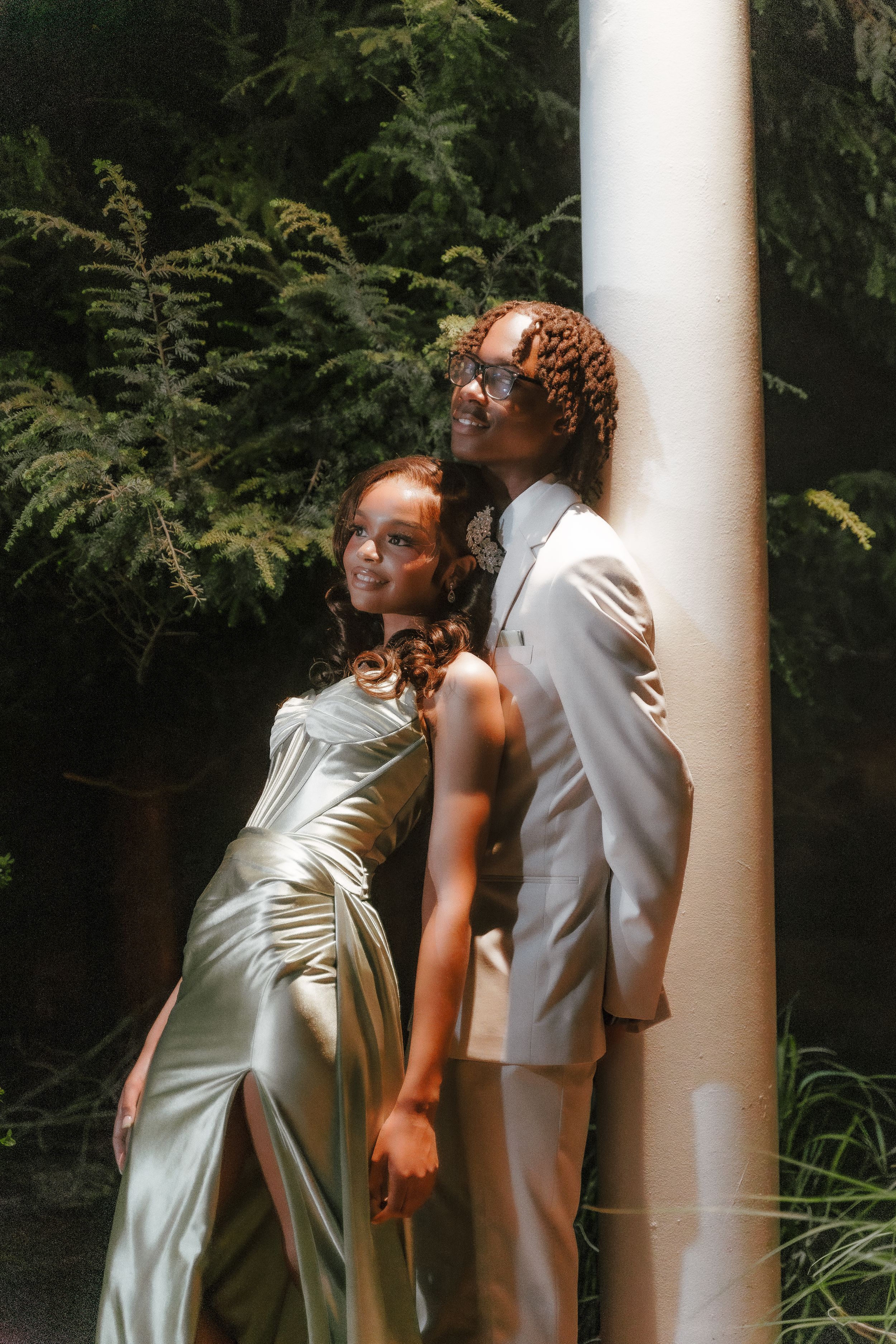 Stylish couple in white formal wear posing against column outdoors.