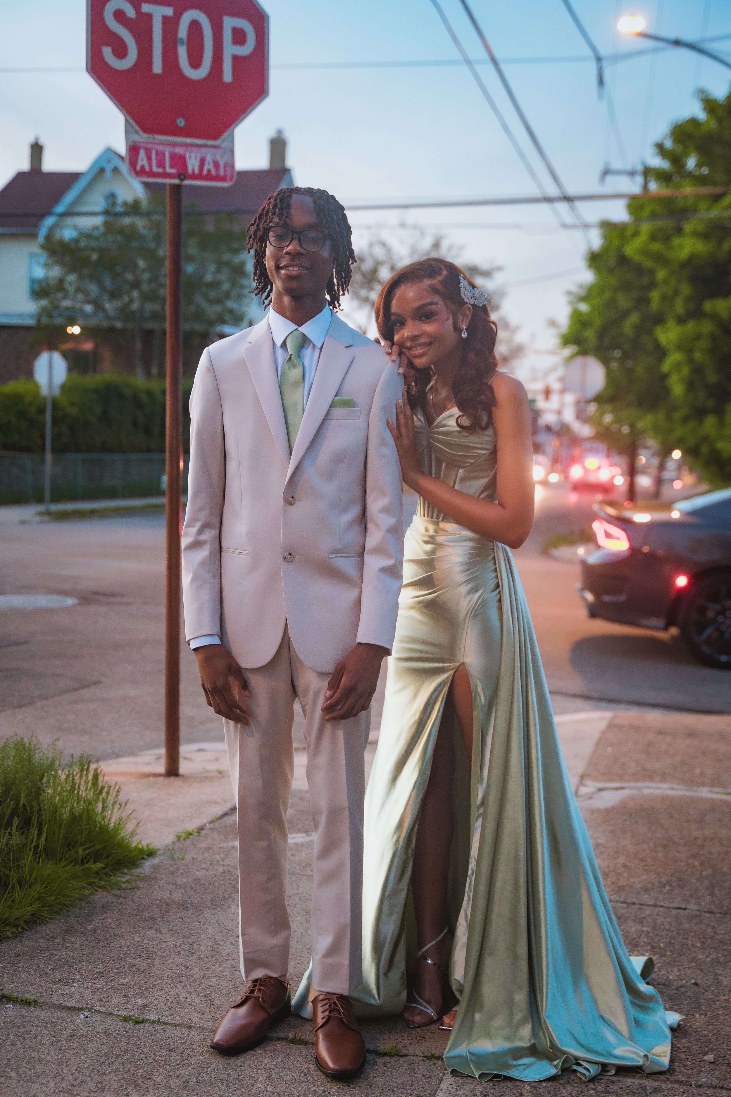 Couple in formal attire posing by stop sign at sunset.