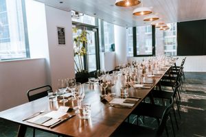 Long dining table set with glasses and place settings in modern room with large windows.