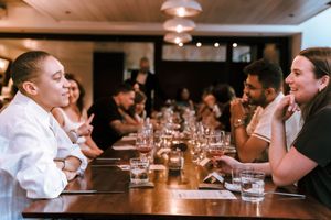 Diners engaged in conversation at a long communal table in a restaurant setting.
