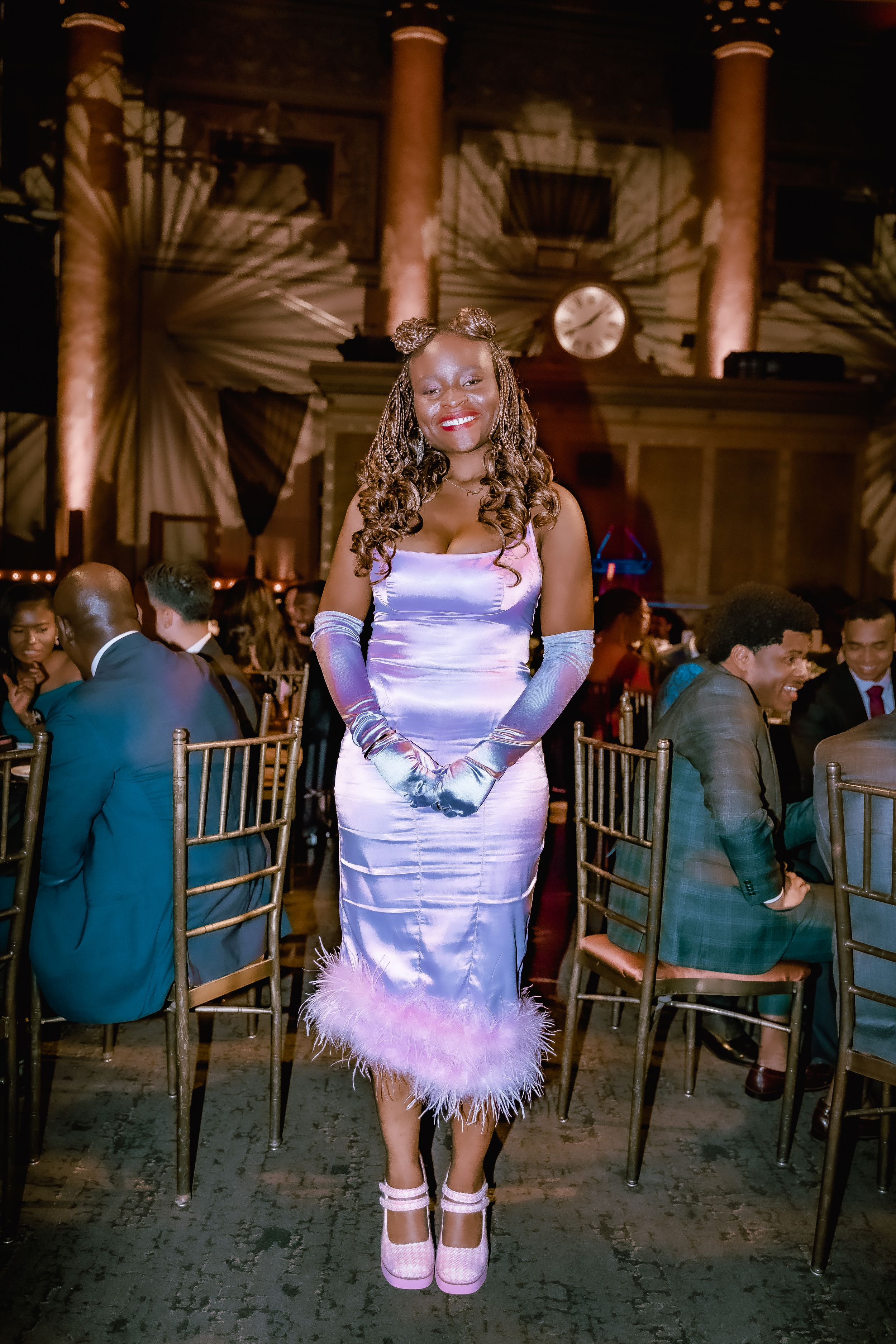 Attendee in a lilac satin dress with feather trim poses at a formal evening event.