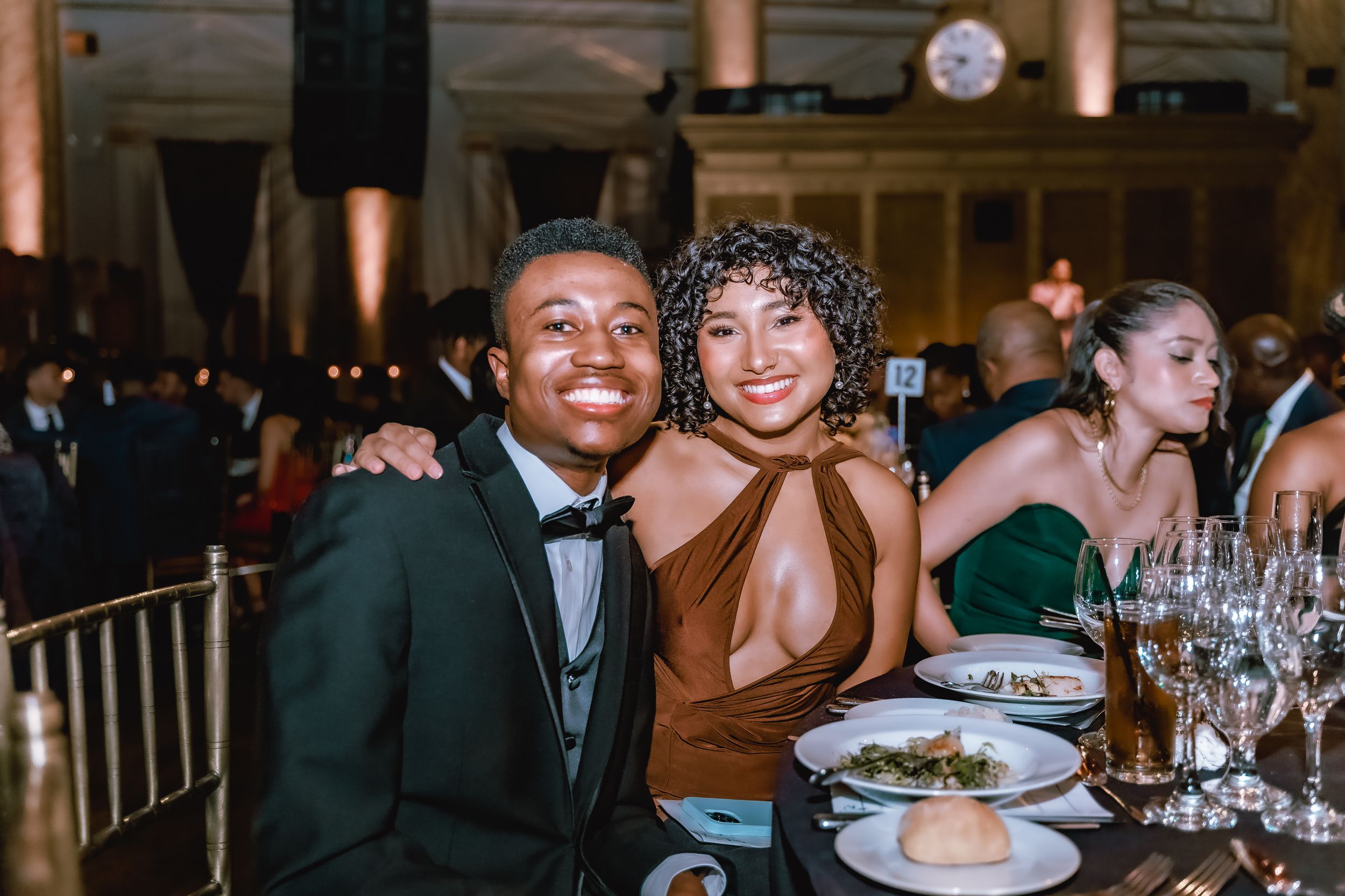 Couples enjoying a formal dinner event at an elegant venue with ornate columns.