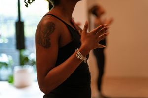 Close-up of hands and bracelet against dark workout attire in a fitness studio setting.