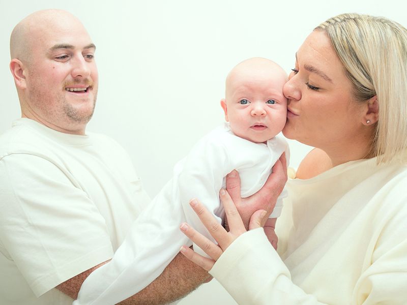 A couple shares a sweet kiss with their newborn baby, beautifully photographed by Abigail's Studio in Buckinghamshire.