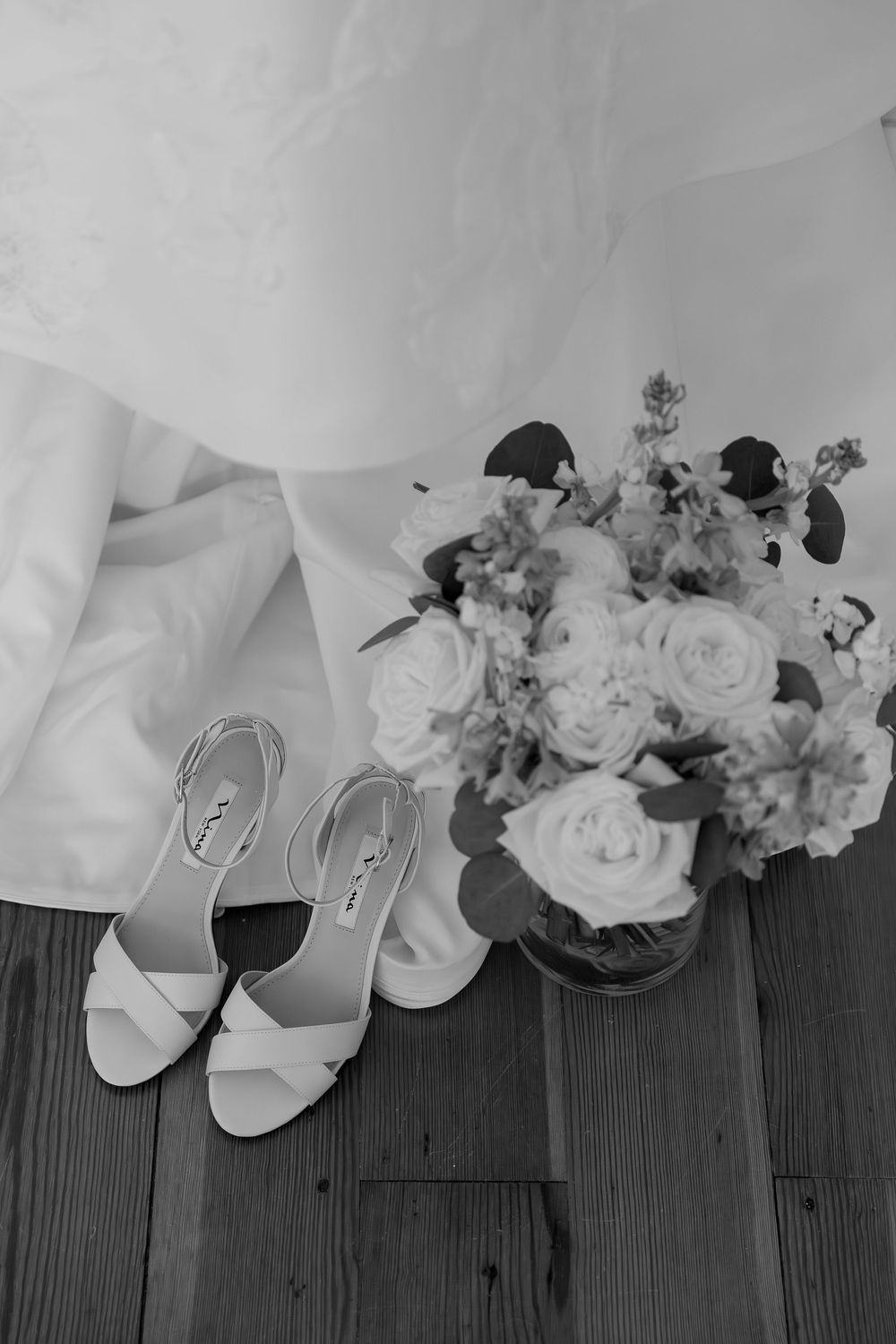White bridal shoes and delicate floral arrangements laid out on dark wooden flooring.