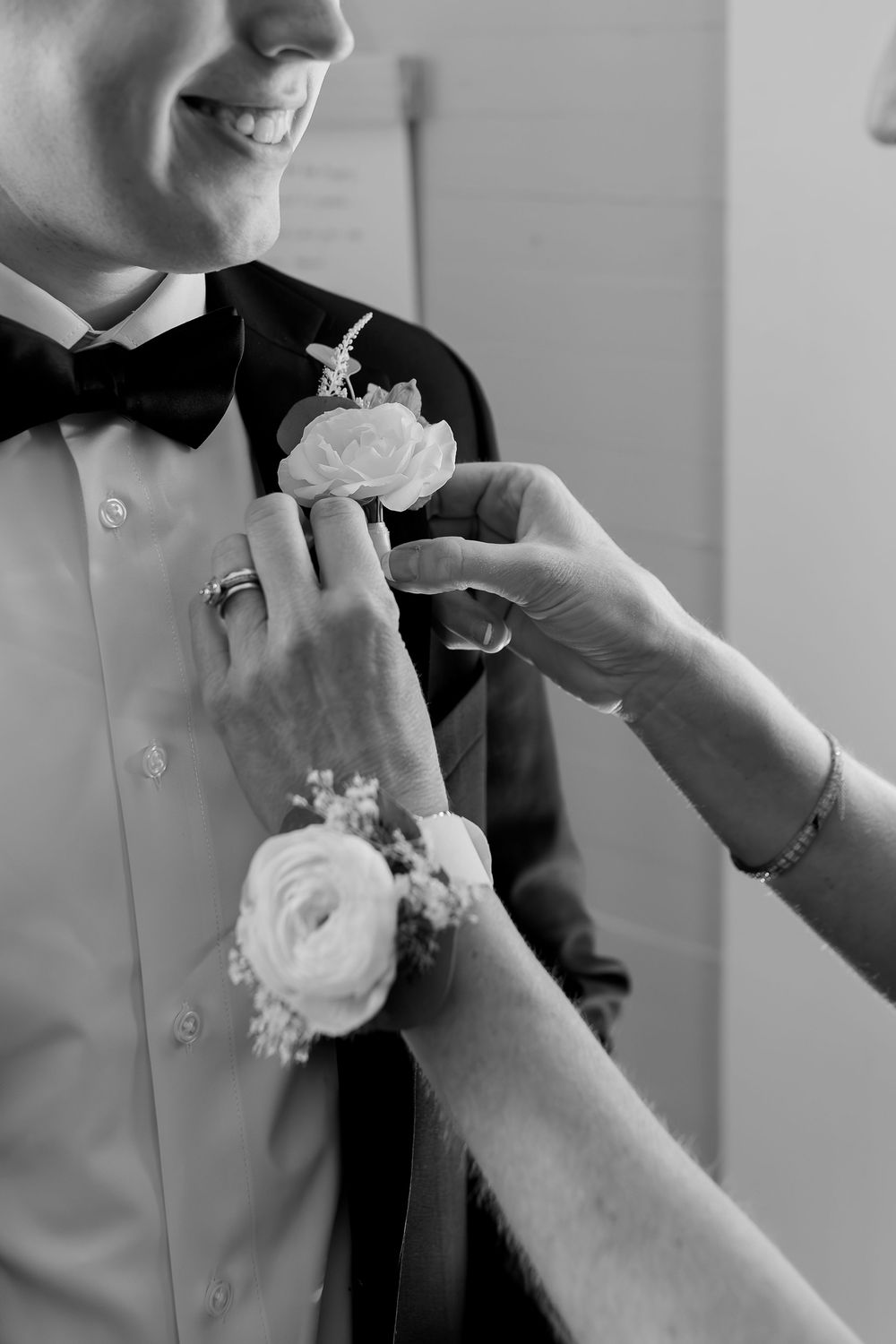 Black and white photo of hands pinning boutonniere flower on lapel.
