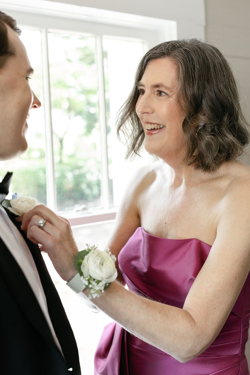 Bridesmaids wearing magenta strapless dresses laugh together in a brightly lit room during a wedding celebration.