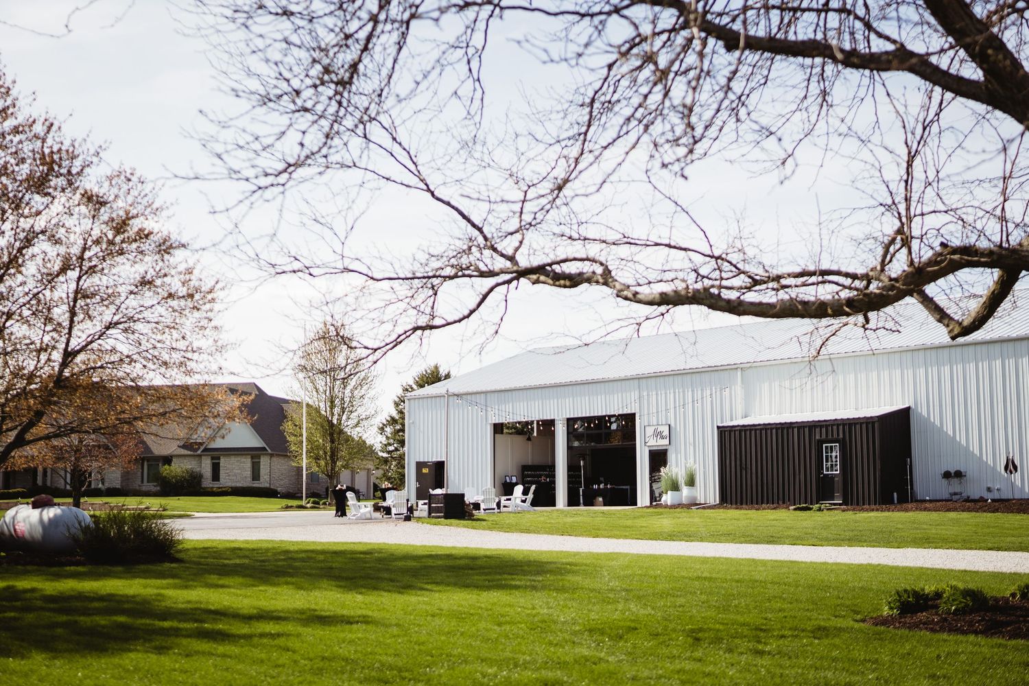 A modern white and black barn-style event venue with large glass doors sits on a manicured green lawn.