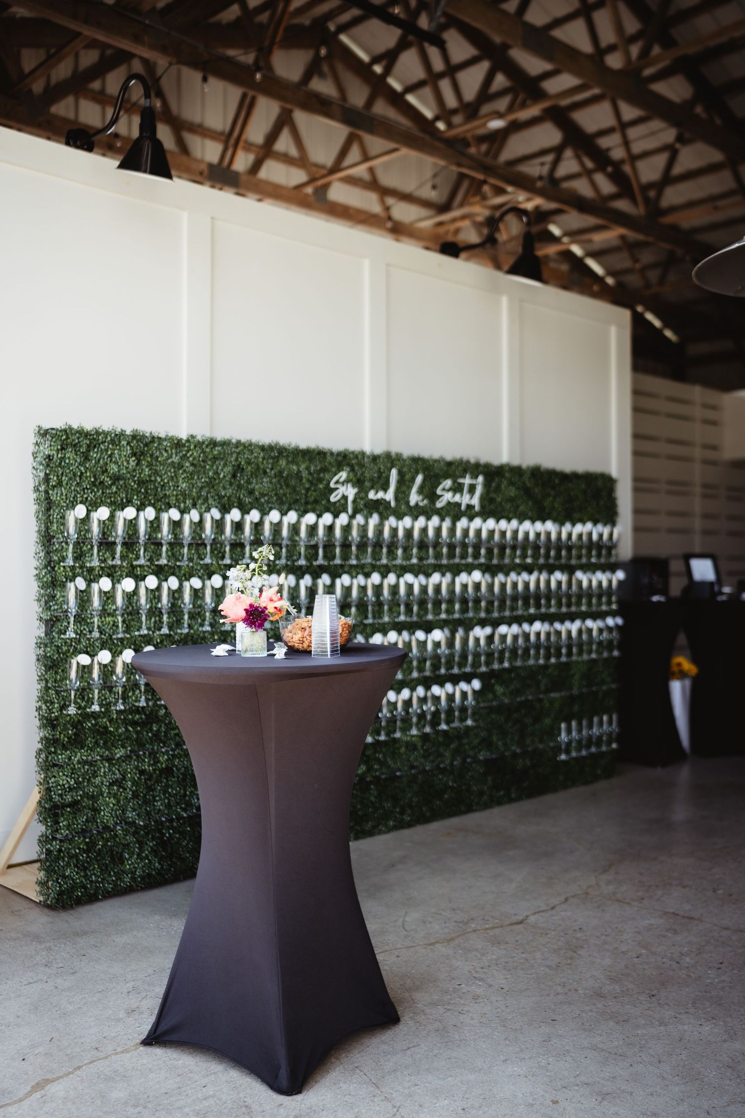 Event seating chart wall display with artificial grass backdrop and cocktail table featuring white escort cards arranged in rows.