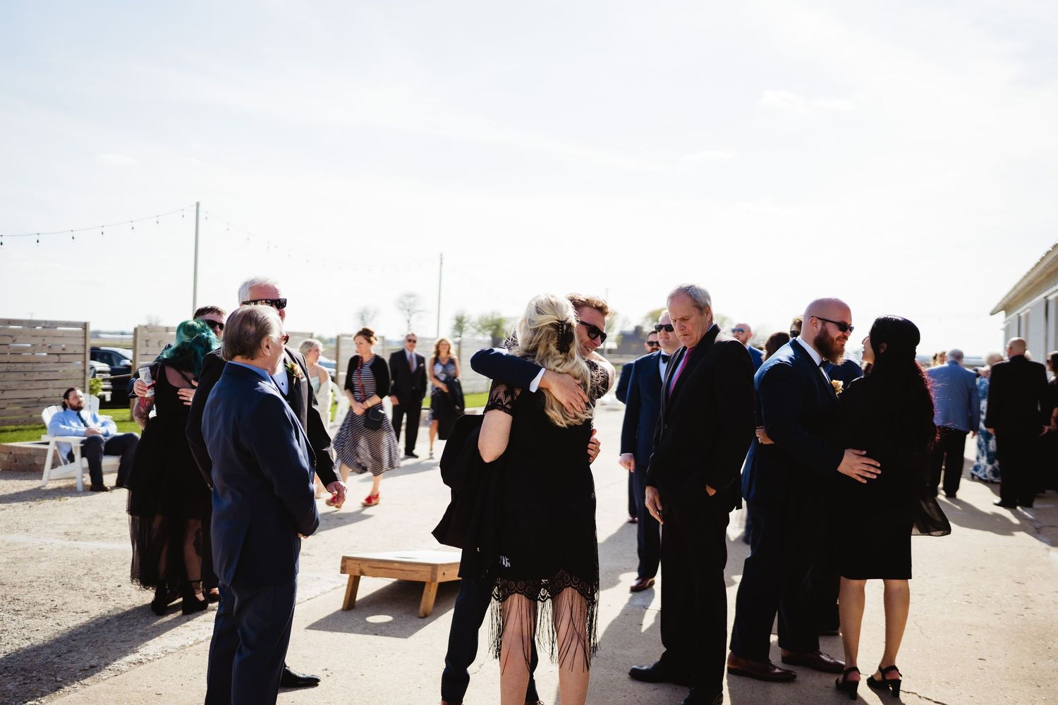 Wedding guests gather outdoors in formal attire during a daytime reception celebration.