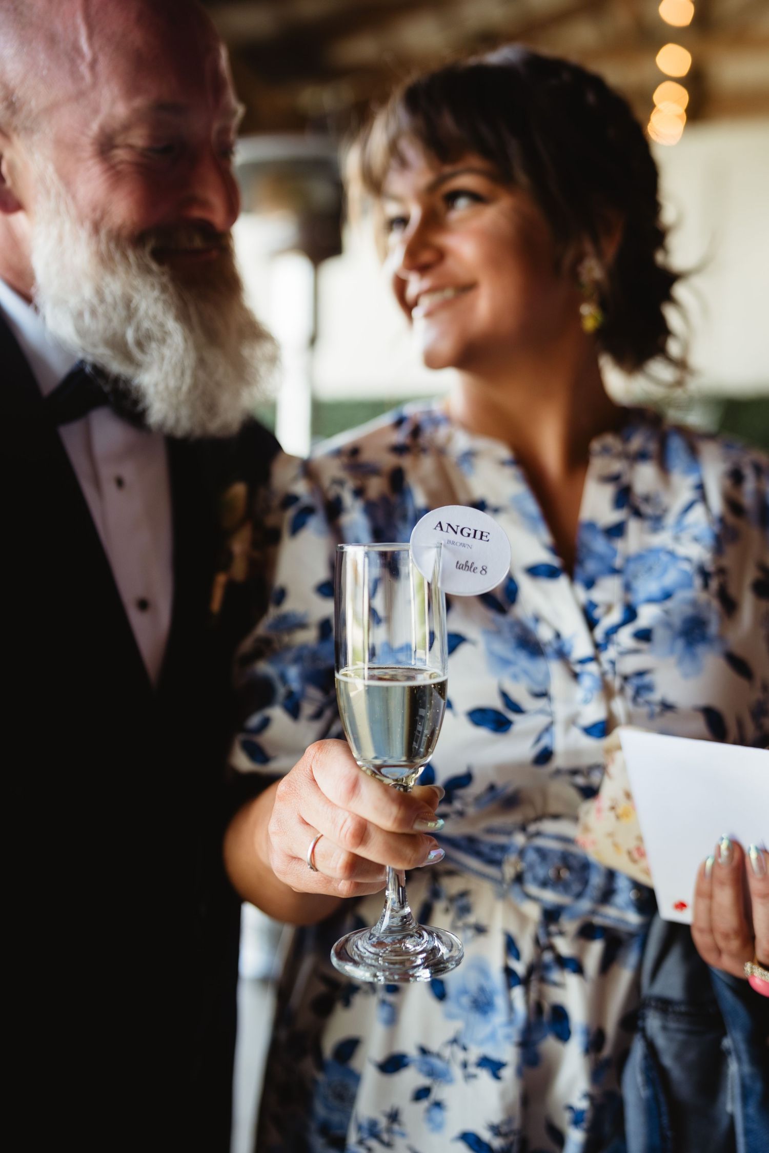 A couple shares an intimate moment at a celebration while holding a champagne flute and wearing formal attire.