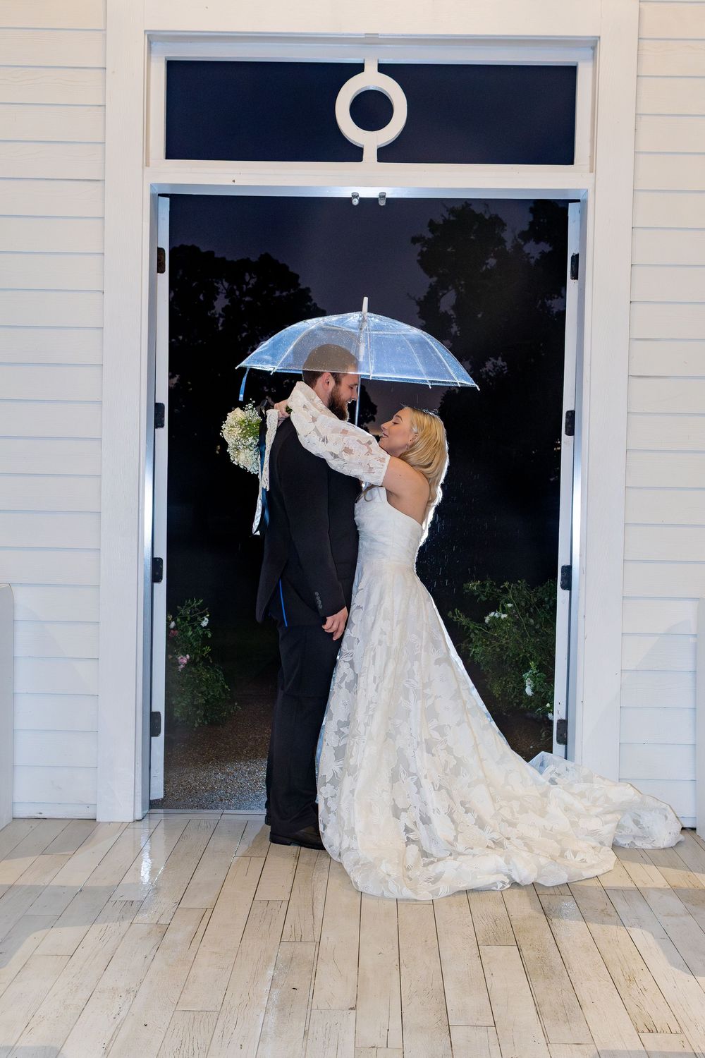 Romantic wedding couple under clear umbrella in doorway.