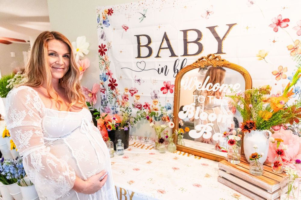 A baby shower celebration setup with floral decorations, a white tablecloth, and an ornate gold mirror display in soft pink tones.