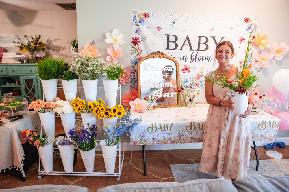 Floral baby shower decor features delicate blooms, white banners, and soft pastel decorations arranged on rustic tables.