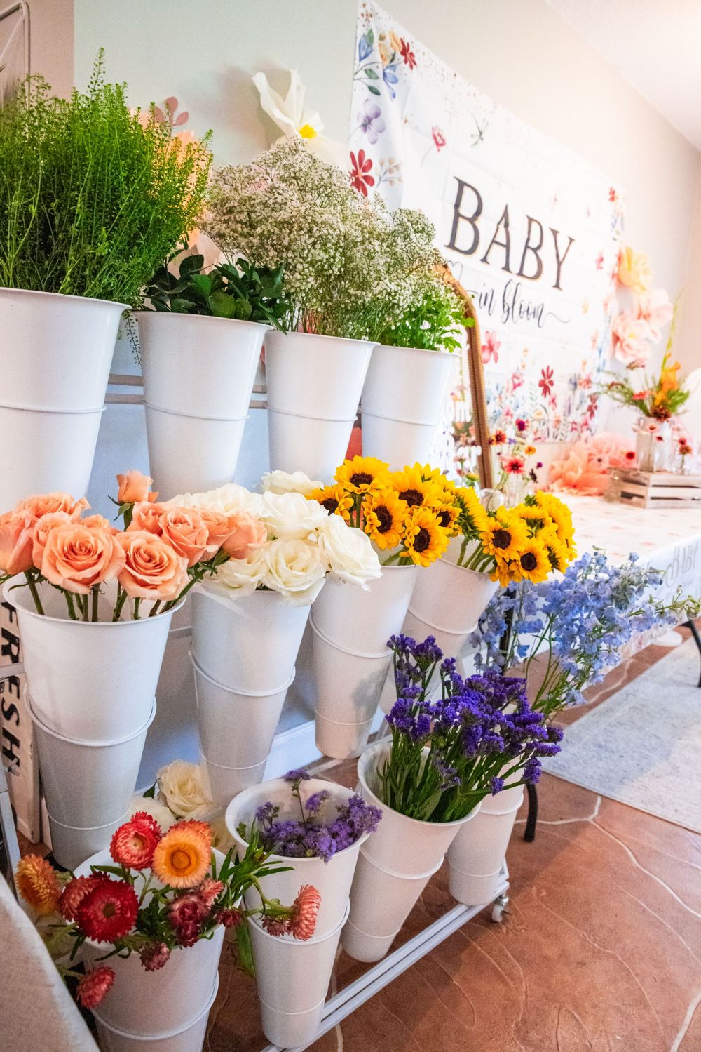 White buckets filled with fresh flowers including sunflowers and roses displayed at Baby Shower event.