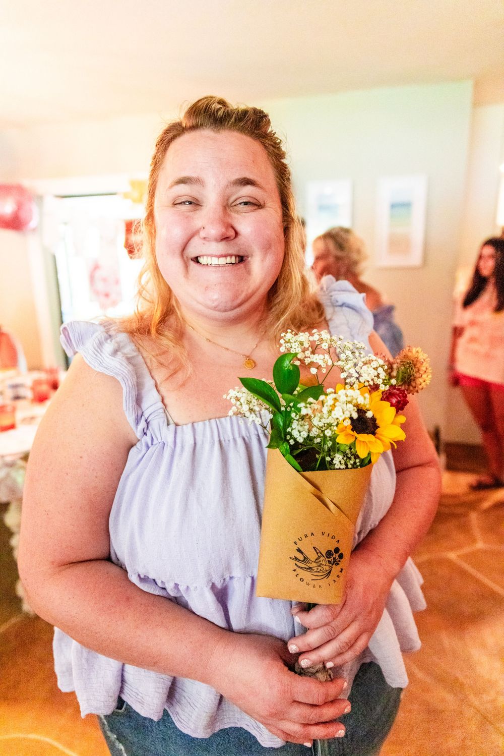 Woman holds beautiful bouquet with sunflowers and baby's breath at indoor celebration.