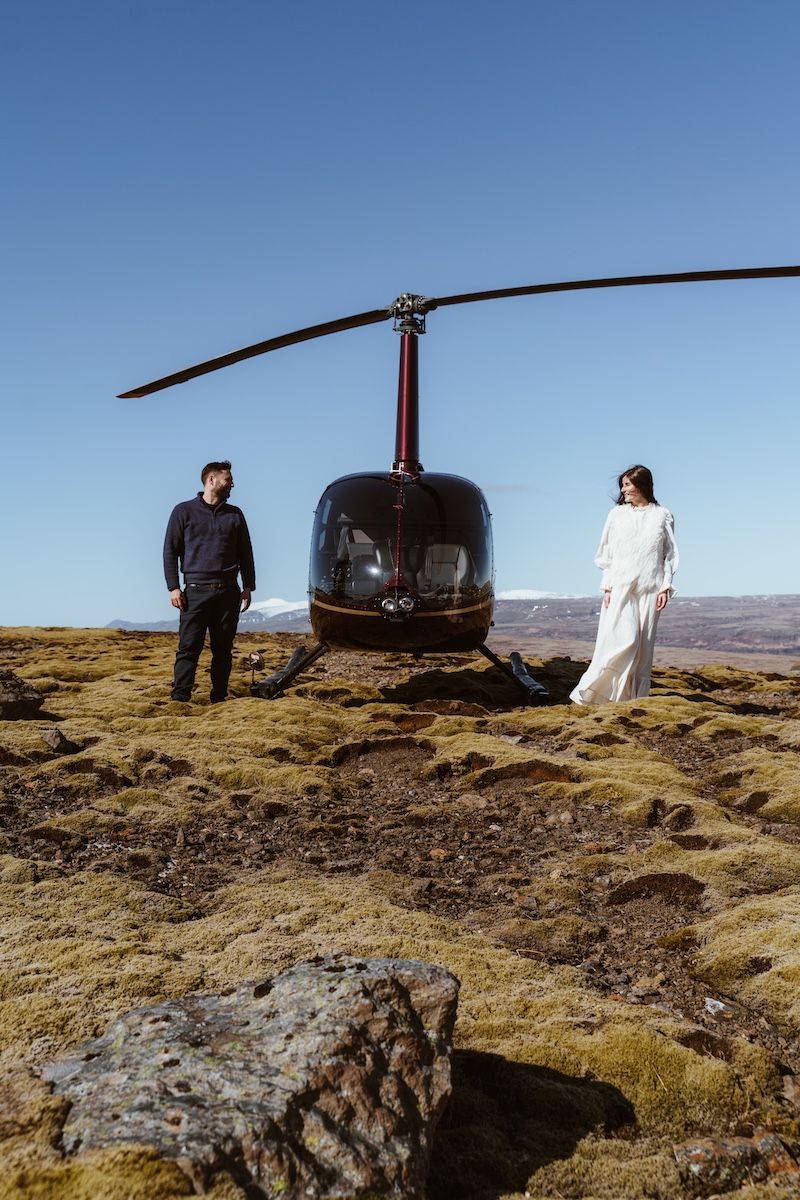 Couple standing next to a helicopter on a moss field.