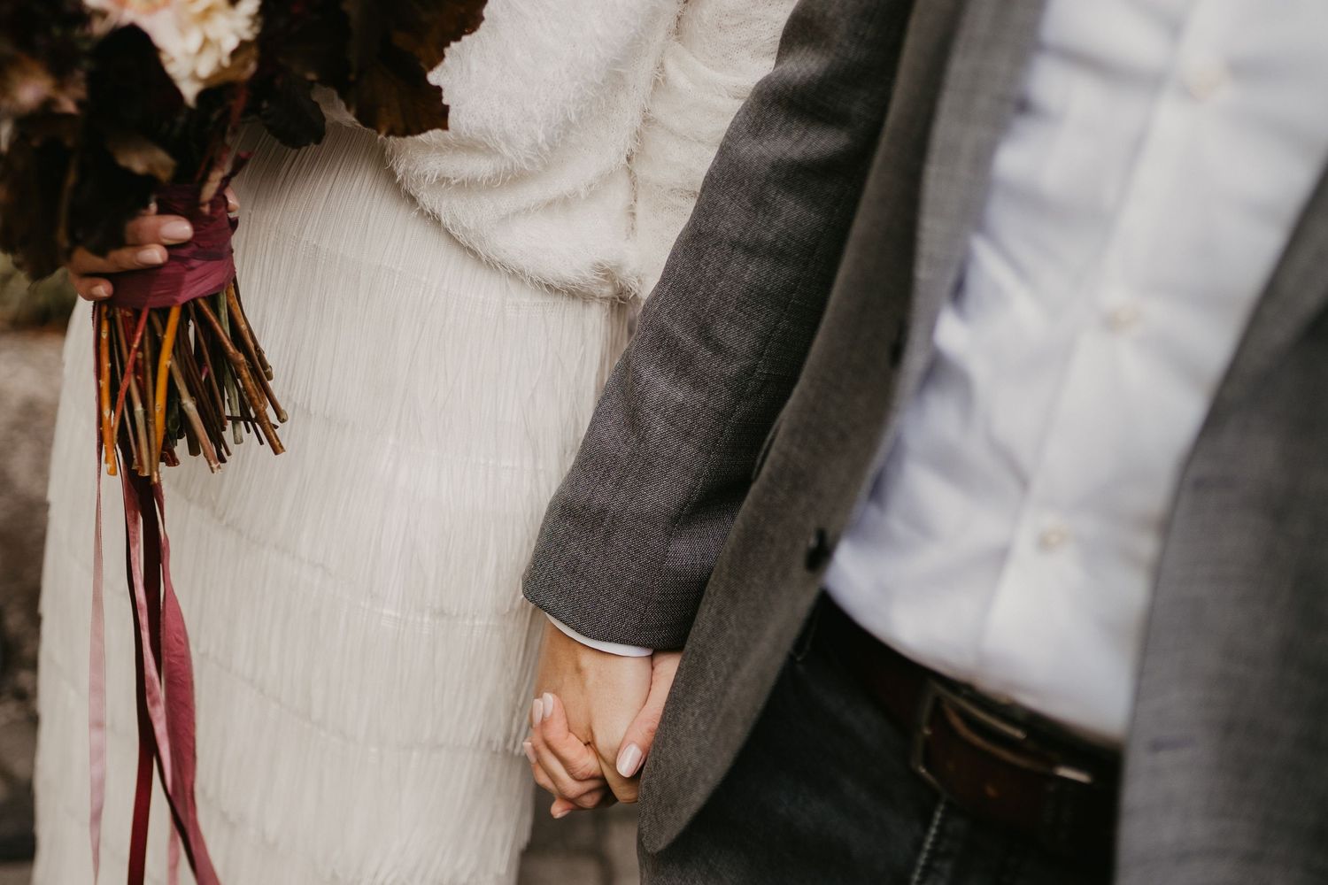 Elegant couple holding hands in formal attire at outdoor celebration.