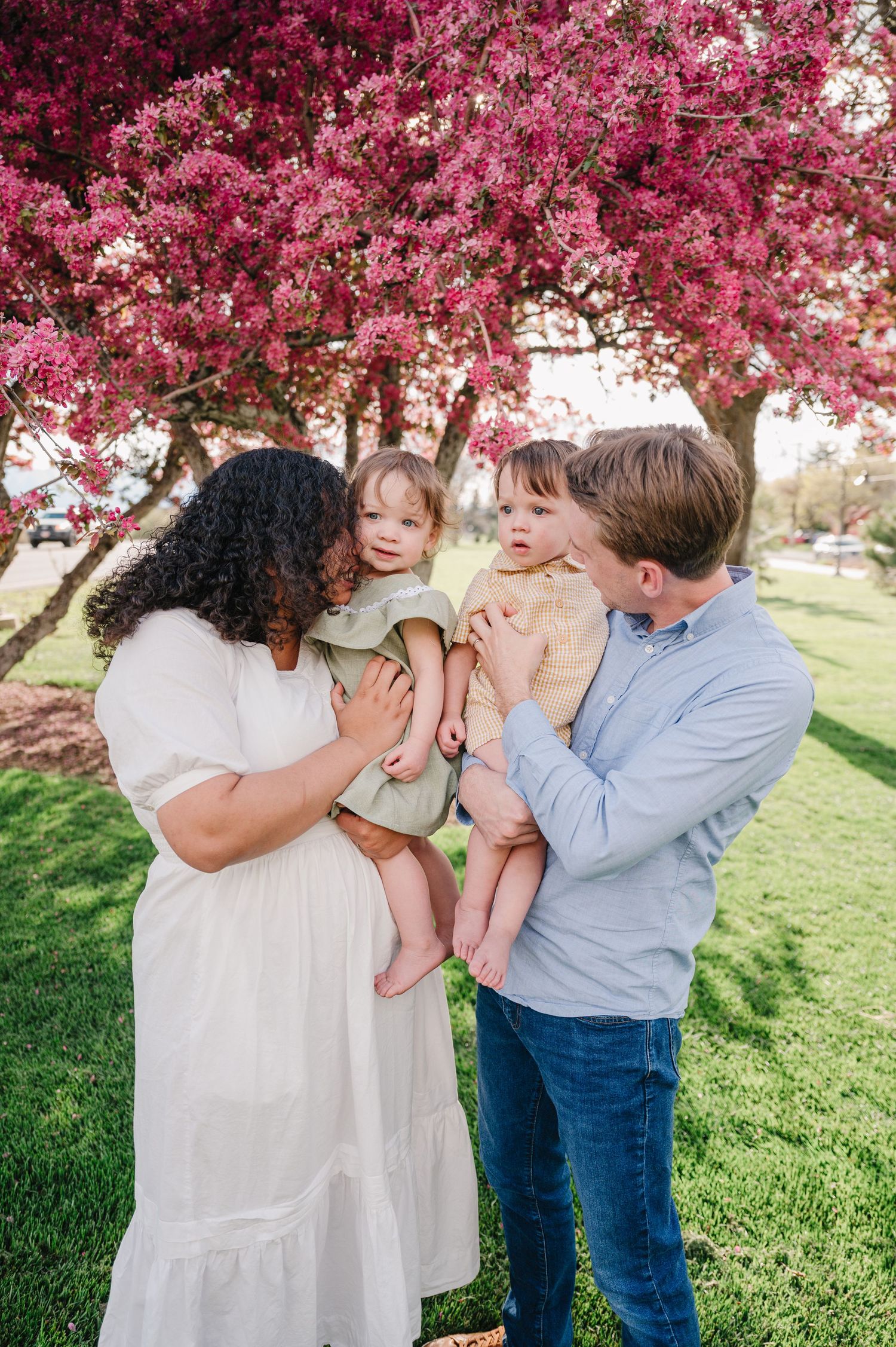A loving family poses together under blooming pink cherry blossoms in a springtime park.