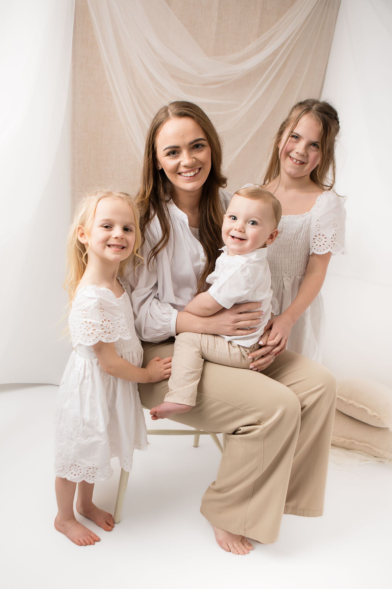 Four people in coordinated white and beige outfits pose together against a light backdrop for a studio portrait.