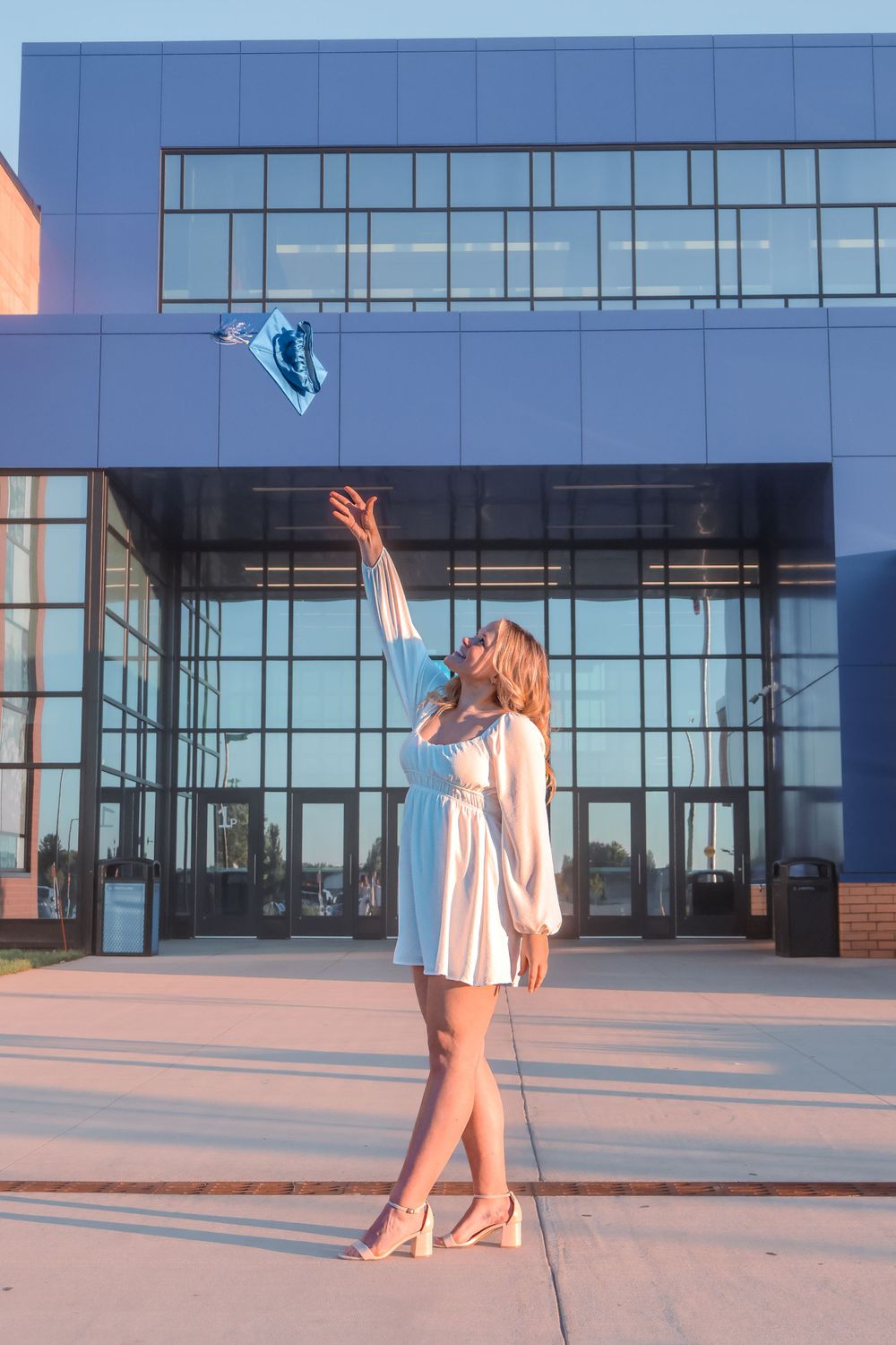 A graduation cap is tossed in the air against a modern glass building backdrop.
