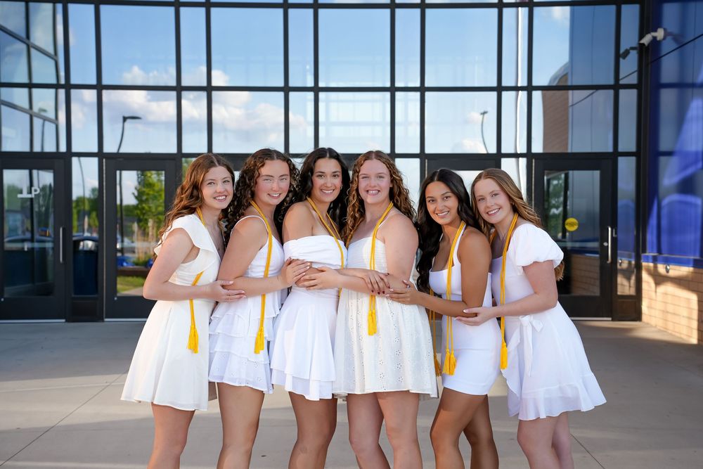 A group of people wearing white dresses pose together in front of a modern building entrance.