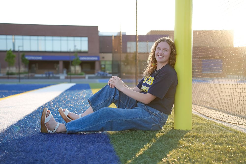 Students relax and socialize on a grassy area outside a school building during golden hour sunset.