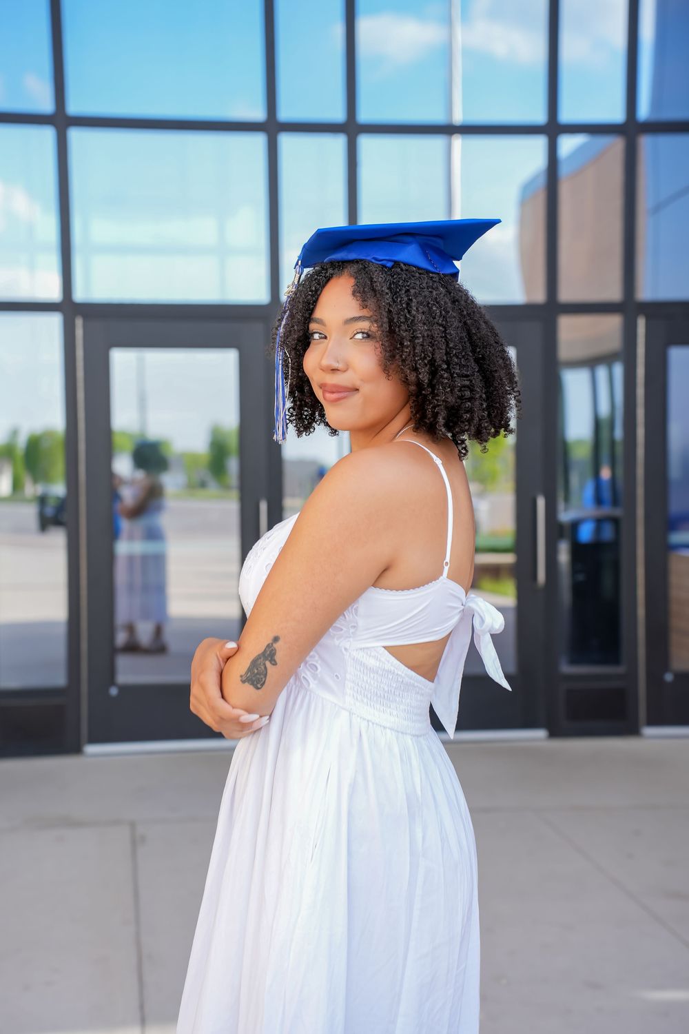 A person in a flowing white dress poses gracefully against a modern glass building exterior.