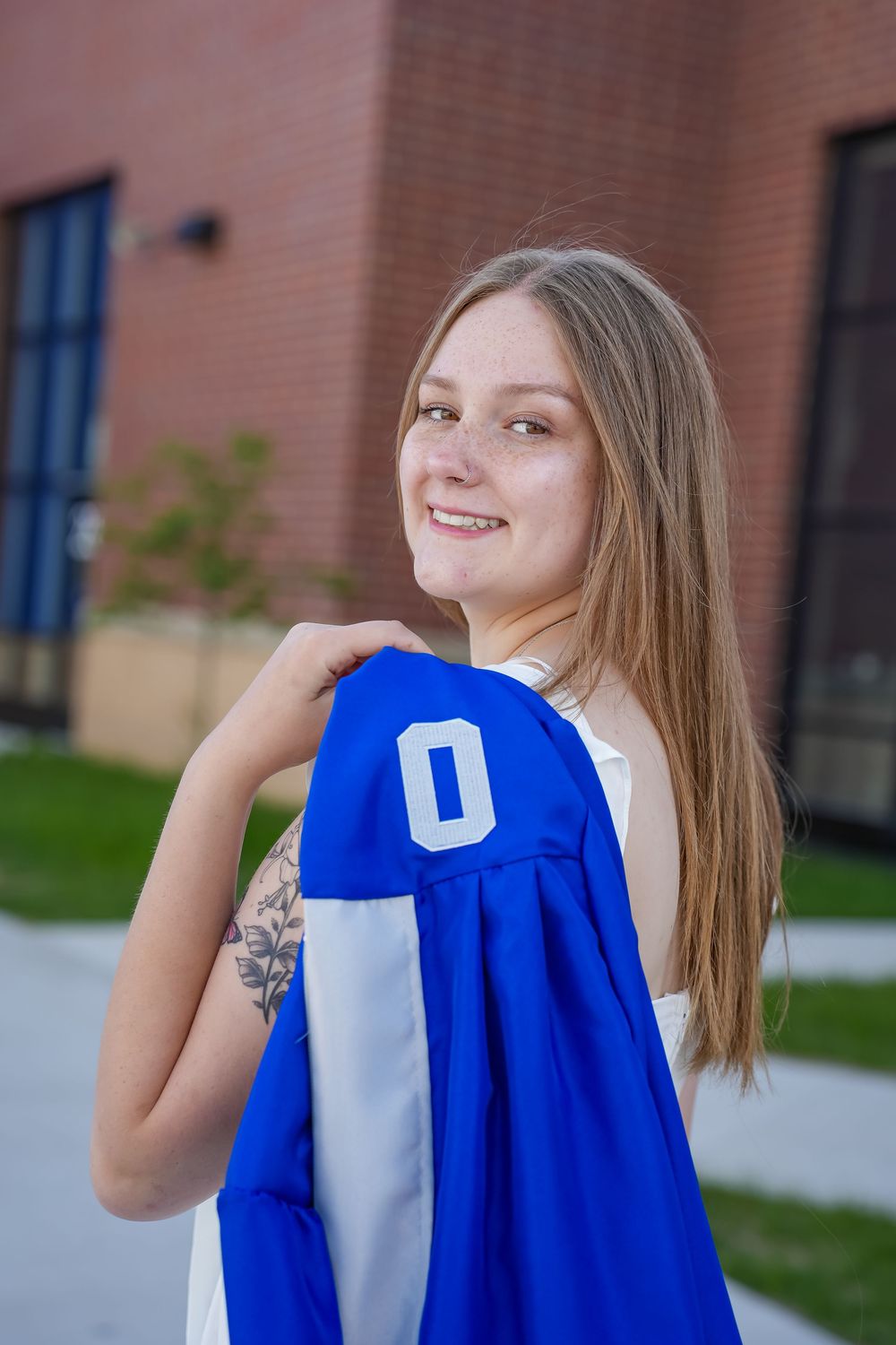 Graduate in blue cap and gown poses outdoors in a series of celebratory shots near brick building.