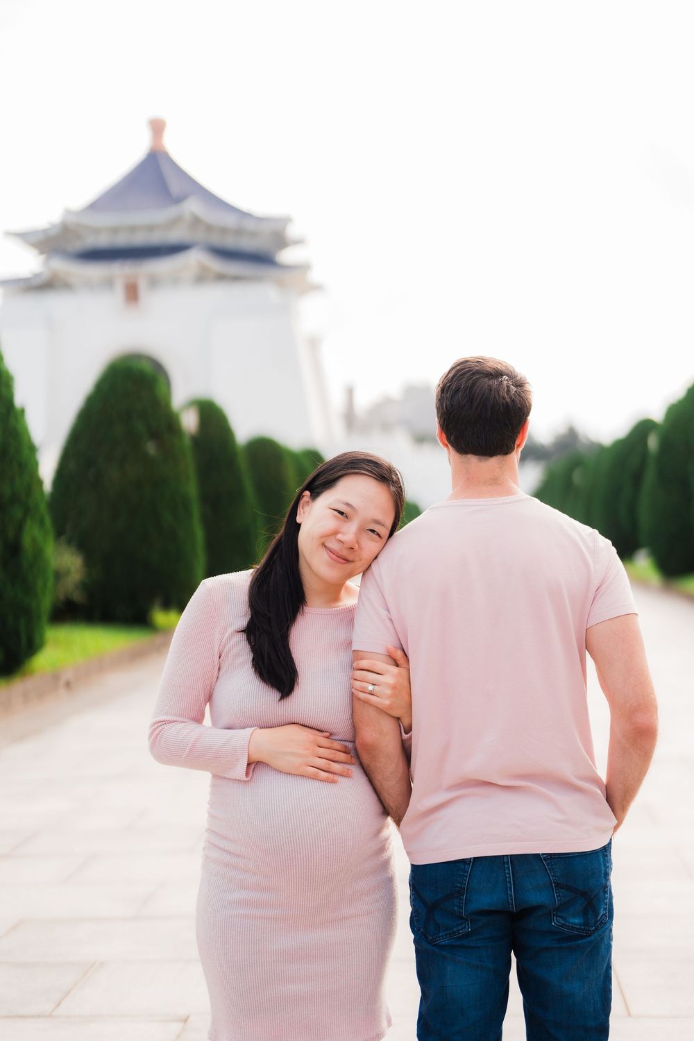 A pregnant couple poses in front of Chiang Kai-shek Memorial Hall in Taipei, Taiwan wearing matching pink tops.